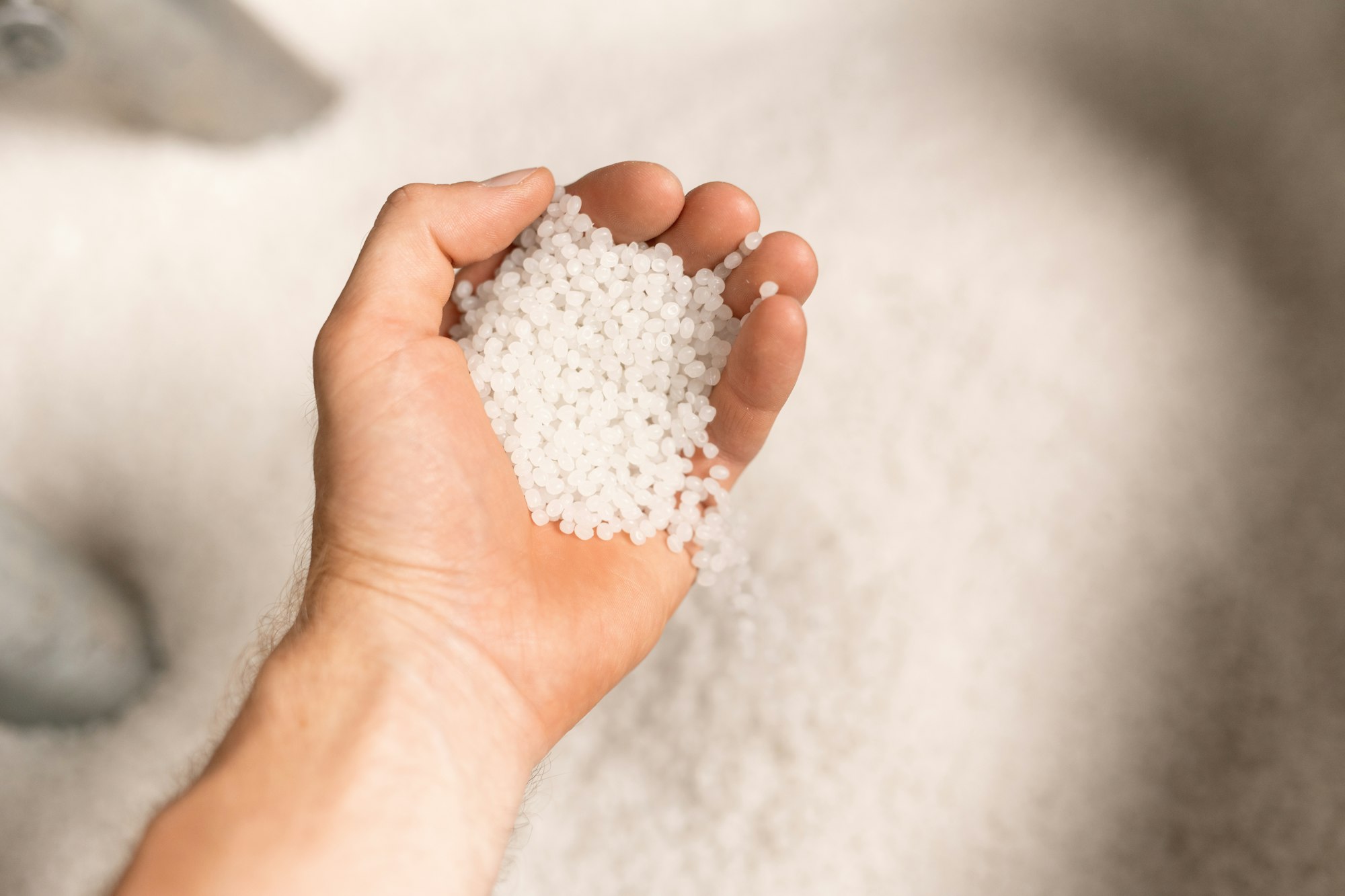 Hand of young male worker of large modern factory holding polymer granules