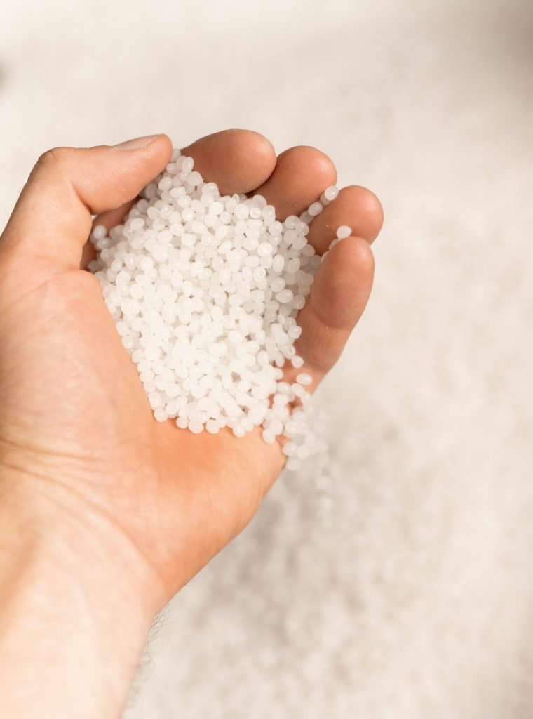 Hand of young male worker of large modern factory holding polymer granules